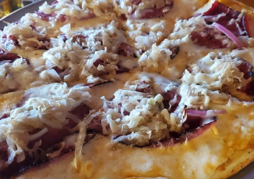 Close-up of a pizza topped with melted cheese, sauerkraut, and slices of meat.