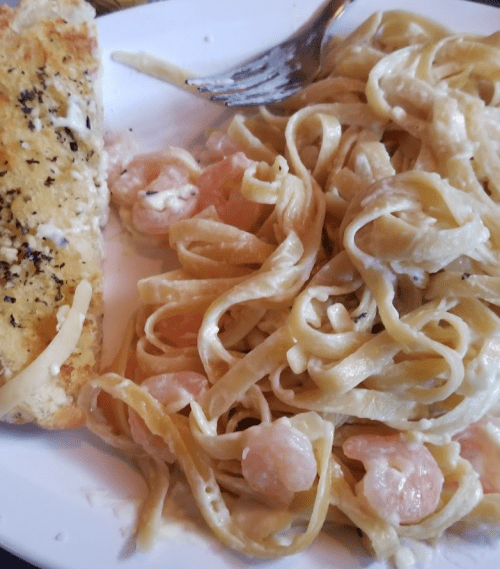 A plate of fettuccine pasta with shrimp in creamy sauce, accompanied by a slice of garlic bread.