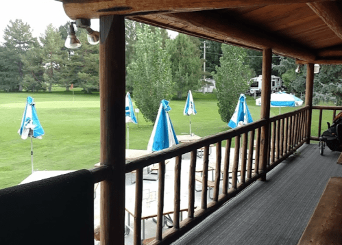 View from a wooden balcony overlooking a green golf course with blue umbrellas and trees in the background.