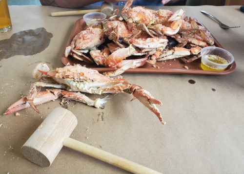 A platter of crabs with a wooden mallet and dipping sauce on a table covered in brown paper.
