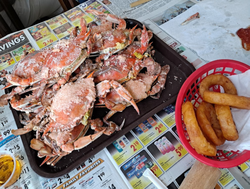 A tray of seasoned crabs on a table, accompanied by a basket of fried dough and dipping sauce.