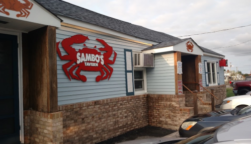 Exterior of Sambo's Tavern featuring a red crab sign, wooden accents, and parked cars in front.