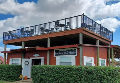 A red building with a sign reading "Southern Hill Market" and a rooftop deck with chairs, surrounded by greenery.