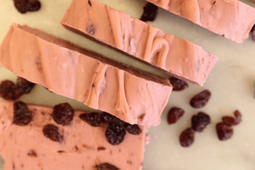 Slices of pink dessert with a creamy texture, scattered with dried cranberries on a light surface.