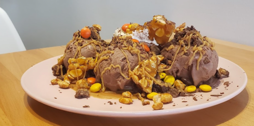 A plate of chocolate ice cream scoops topped with caramel, nuts, chocolate shavings, and colorful candy.