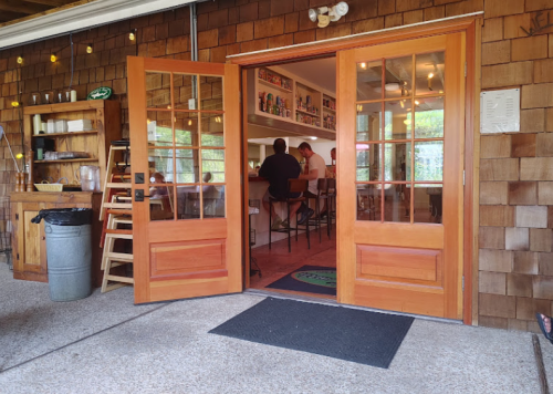 Open double doors leading into a cozy bar area with patrons seated at the counter, surrounded by wooden decor.