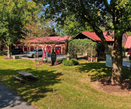 A scenic view of a building with a red roof, surrounded by trees and a grassy area with picnic tables.