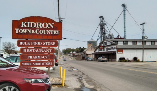Sign for Kidron Town & Country with directions to a bulk food store, restaurant, pharmacy, and work shoe store.