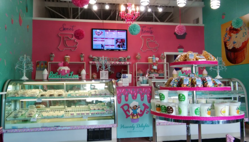 Brightly colored dessert shop interior with display cases, a menu screen, and decorative elements like pom-poms and a chandelier.