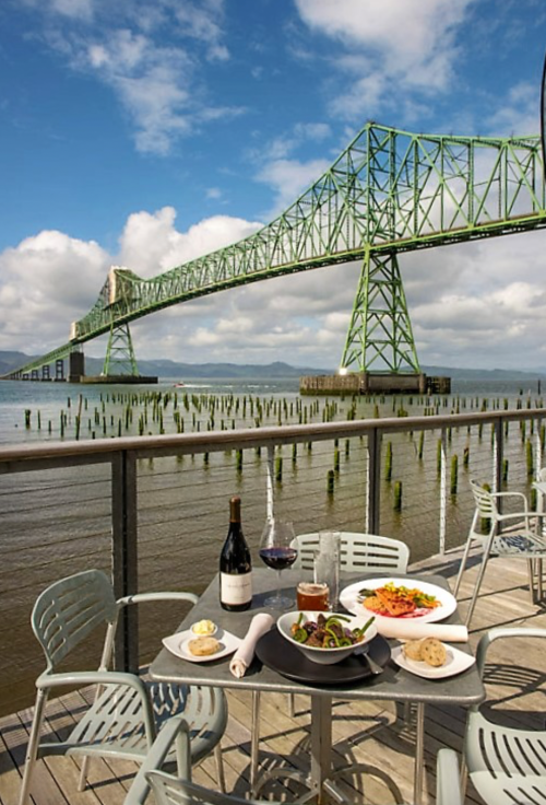 A scenic view of a bridge over water, with a table set for dining featuring wine and a colorful meal.