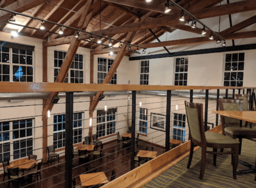 Interior of a spacious restaurant with wooden beams, large windows, and tables arranged on a polished floor.