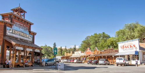 A charming street scene featuring wooden storefronts, including an emporium and a saloon, under a clear blue sky.
