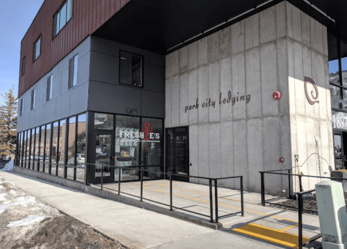 Exterior view of Park City Lodging with large windows and a Freshie's store entrance, featuring a ramp and snow on the ground.