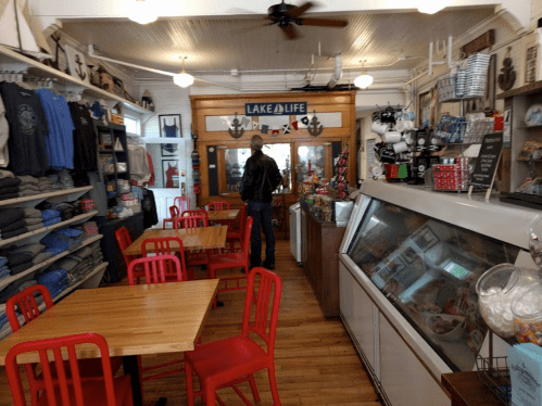 A cozy shop interior with red chairs, wooden tables, and shelves filled with merchandise. A person browses near the entrance.