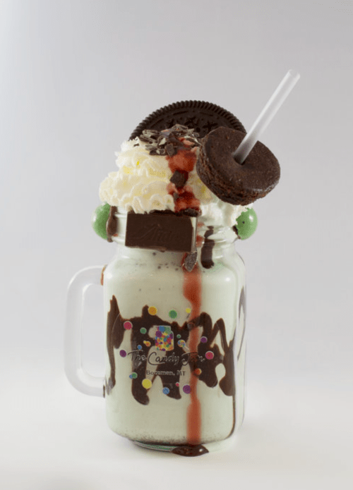 A decadent milkshake topped with whipped cream, an Oreo, chocolate drizzle, and a straw in a mason jar.
