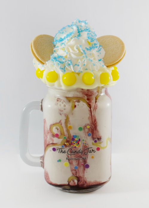 A colorful milkshake topped with whipped cream, blue sprinkles, cookies, and candy in a glass jar.