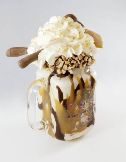 A decadent milkshake topped with whipped cream, chocolate drizzle, caramel, and candy pieces in a glass jar.