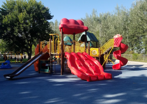 Colorful playground with slides and climbing structures, surrounded by trees and a clear blue sky.