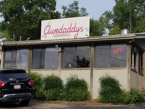 Exterior of Awedaddys Food & Spirits, featuring a sign and a car parked outside, surrounded by greenery.