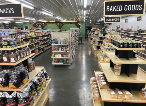 A well-organized grocery store aisle featuring snacks, baked goods, and bulk foods on wooden shelves.