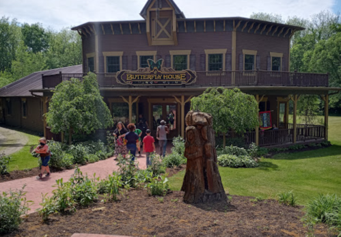 A wooden building with a sign reading "Butterfly House," surrounded by greenery and visitors entering the entrance.