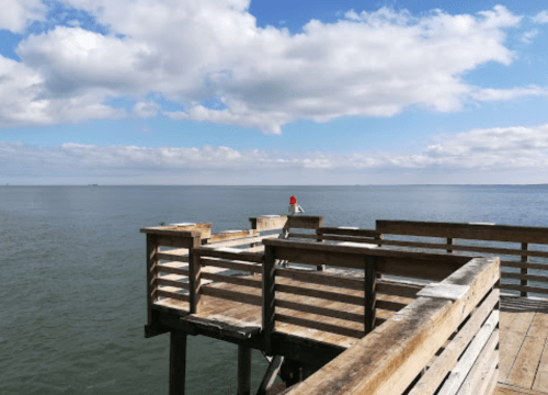 A wooden pier extends over calm water under a partly cloudy sky.