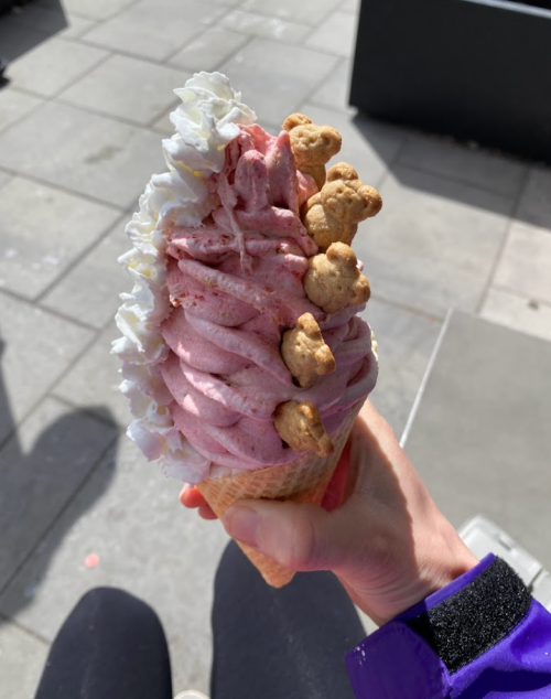 A hand holding a colorful ice cream cone topped with whipped cream and small cookie bears.