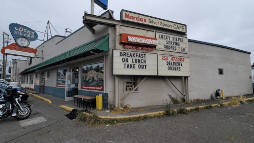 Exterior of Marcia's Silver Spoon Cafe with a sign for takeout and delivery orders, featuring a motorcycle parked outside.
