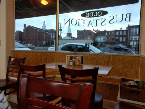 View from inside a diner with wooden tables and chairs, looking out at a street and buildings through a large window.