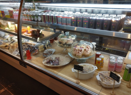 A display case filled with various desserts, pastries, and drinks, showcasing colorful treats and neatly labeled items.