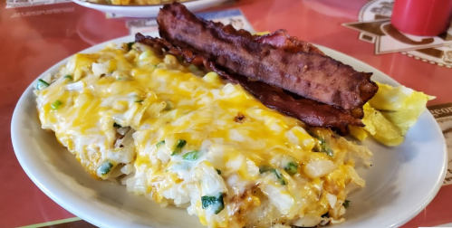 A plate of cheesy hash browns topped with green onions and crispy bacon, served with a lemon wedge.