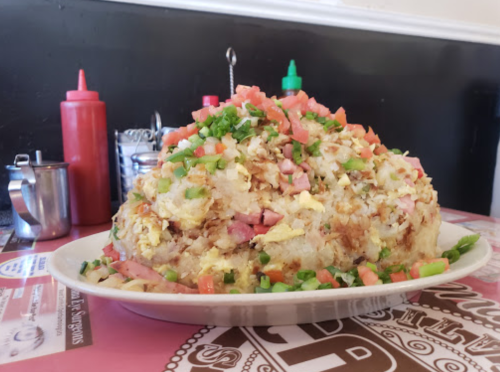 A large plate of fried rice topped with diced vegetables, ham, and green onions, served in a casual dining setting.