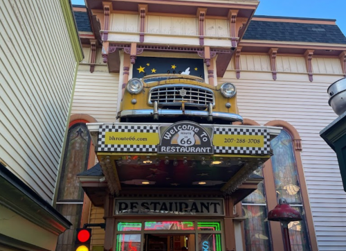 A vintage yellow car is mounted above the entrance of a Route 66-themed restaurant with colorful signage.