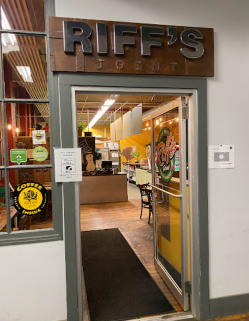 Entrance to Riff's Joint, featuring a wooden sign and a welcoming interior with tables and decor visible.