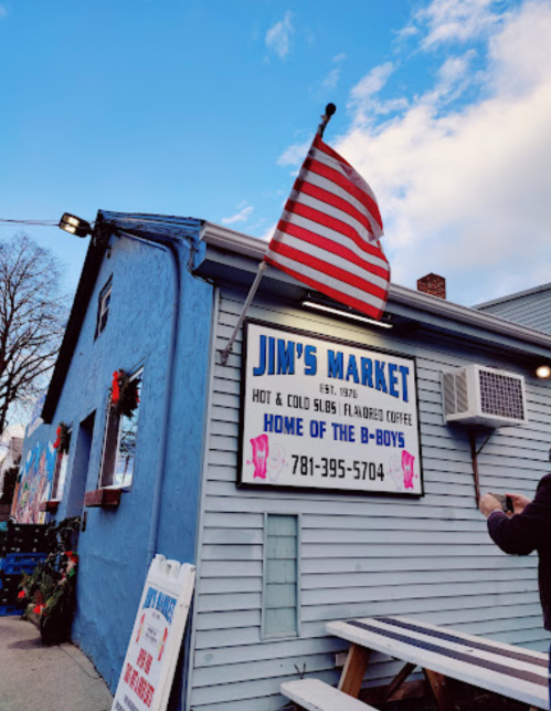 A blue building with a sign for Jim's Market, featuring a U.S. flag and details about hot and cold beverages.