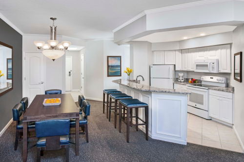 A modern kitchen and dining area with a table, chairs, and bar seating, featuring light colors and elegant decor.