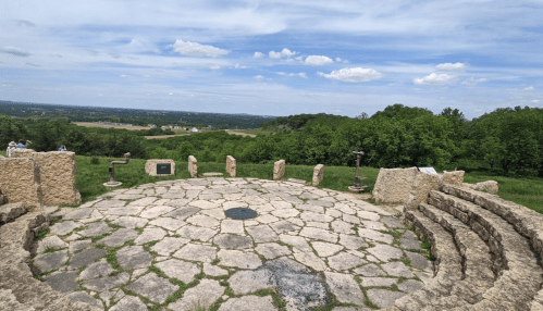 A stone observation area with benches overlooks a lush green landscape under a blue sky with scattered clouds.
