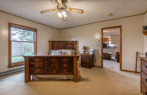 Cozy bedroom with wooden furniture, a ceiling fan, and a view of the outdoors through a large window.
