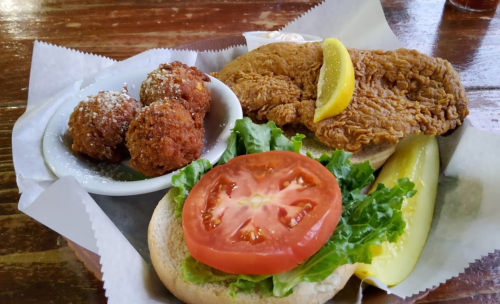 A plate with fried chicken, lettuce, tomato, and lemon, alongside a dish of fried balls dusted with powdered sugar.