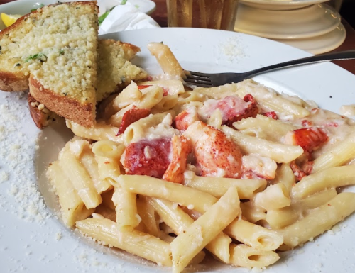 A plate of creamy lobster pasta with penne, served with a slice of garlic bread on the side.