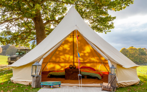 A cozy glamping tent with colorful bedding, lanterns, and a warm glow, set in a scenic outdoor landscape.