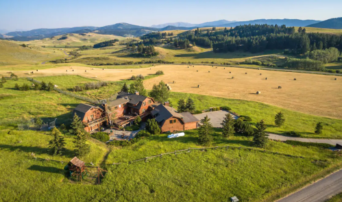 Aerial view of a rustic farmhouse surrounded by green fields and mountains in the background.