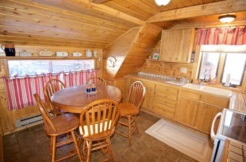 Cozy wooden kitchen with a round table, chairs, and a window, featuring rustic decor and warm lighting.