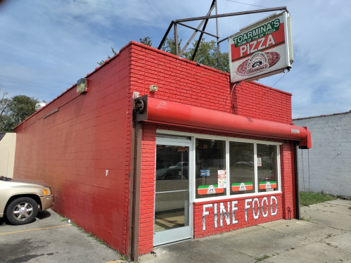 A red brick pizza shop with a sign reading "Toarmina's Pizza" and "Fine Food" on the window.