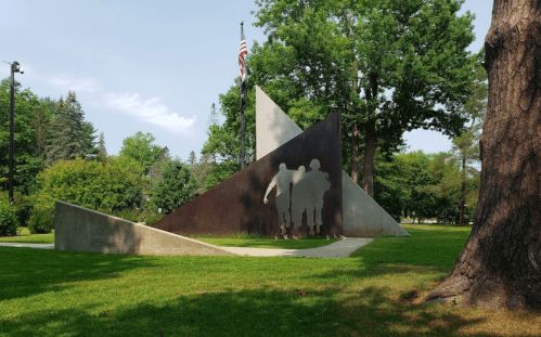 A modern sculpture in a park featuring abstract shapes and silhouettes of three figures against a green landscape.