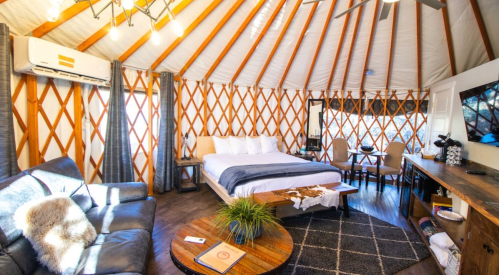 Cozy yurt interior featuring a bed, seating area, dining table, and modern decor with wooden accents.