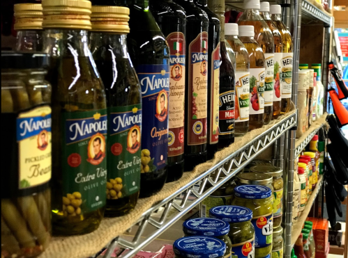 A shelf filled with various bottles of olive oil, vinegar, and pickled goods, showcasing a variety of brands.