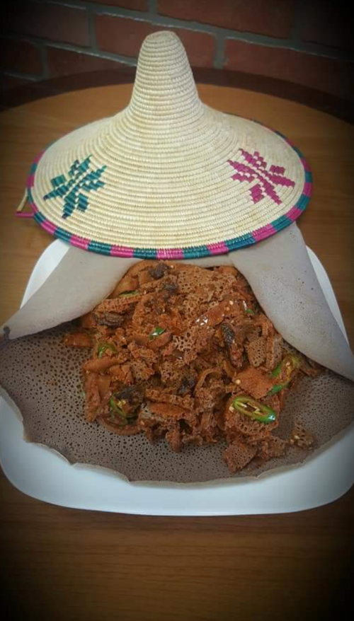 A traditional dish served on a plate, covered with a woven hat, showcasing crispy, spiced food with green peppers.
