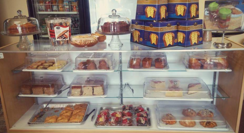 A display case filled with various baked goods, including cakes, pastries, and cookies, under glass covers.