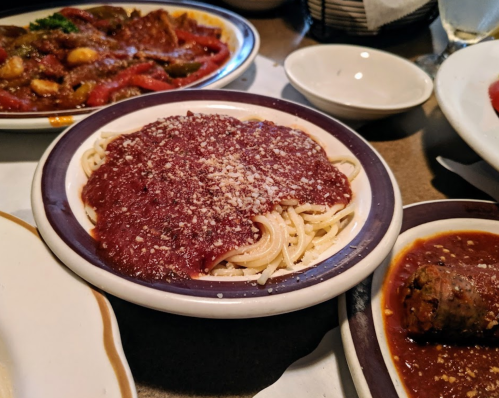 A plate of spaghetti topped with marinara sauce and grated cheese, served alongside other dishes in a restaurant setting.